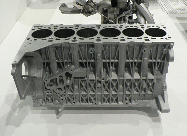 Un bloc moteur m&eacute;tallique &agrave; six cylindres est affich&eacute; sur une surface blanche. La structure, probablement produite par un fournisseur de moulage sous pression en Chine, pr&eacute;sente des motifs g&eacute;om&eacute;triques complexes et divers points de montage, mettant en valeur son ing&eacute;nierie d&eacute;taill&eacute;e. Un assemblage complexe de tuyaux est partiellement visible &agrave; l"arri&egrave;re-plan